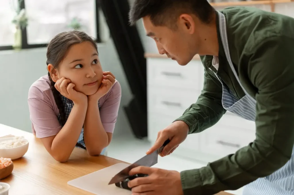 Parent preparing a meal in the kitchen while their child watches attentively, representing everyday parenting responsibilities and hands-on care.