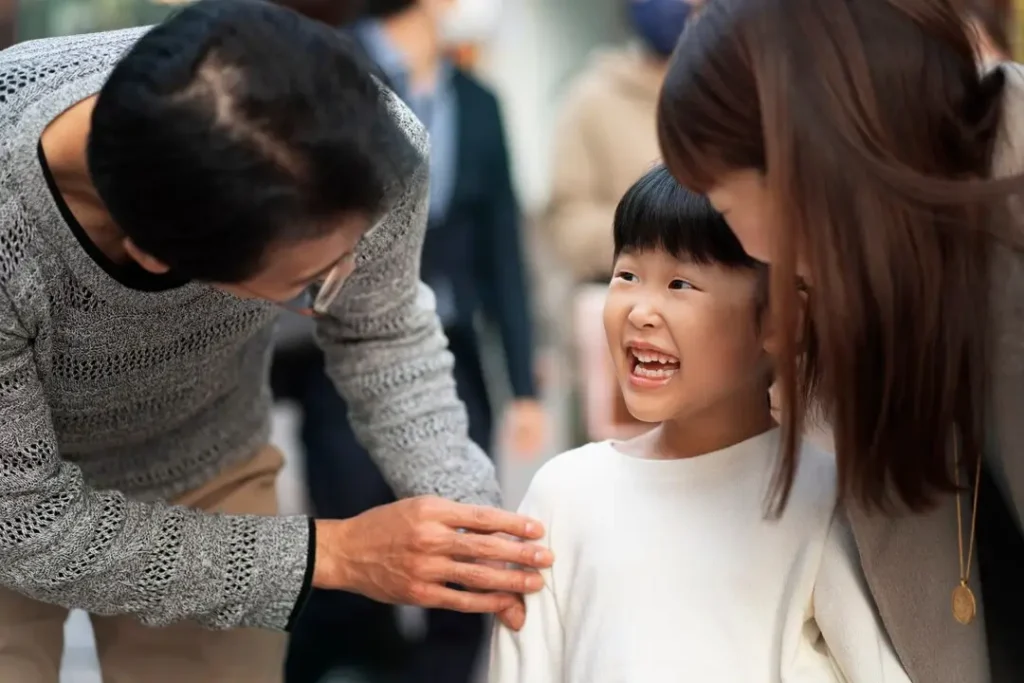 Smiling child standing between two adults who are leaning in supportively, reflecting a caring and involved family environment.