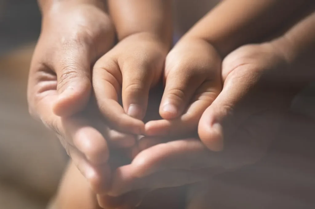 Close-up of a child’s hands resting gently in a parent’s hands, symbolizing protection, guidance, and parental support.