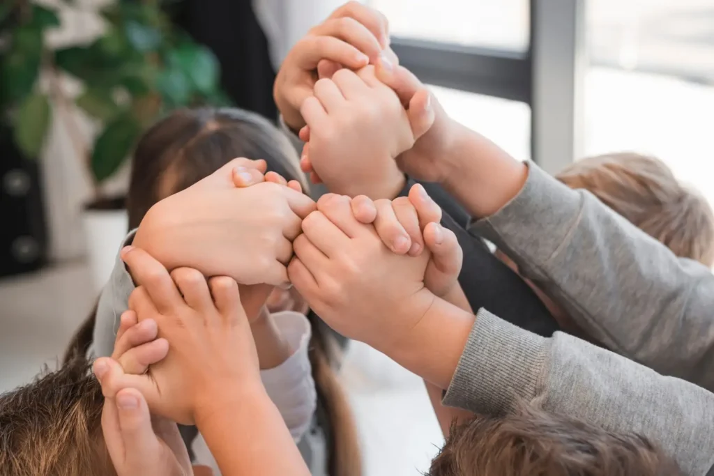 Children stacking their hands together in a group gesture, symbolizing unity, cooperation, and shared support.