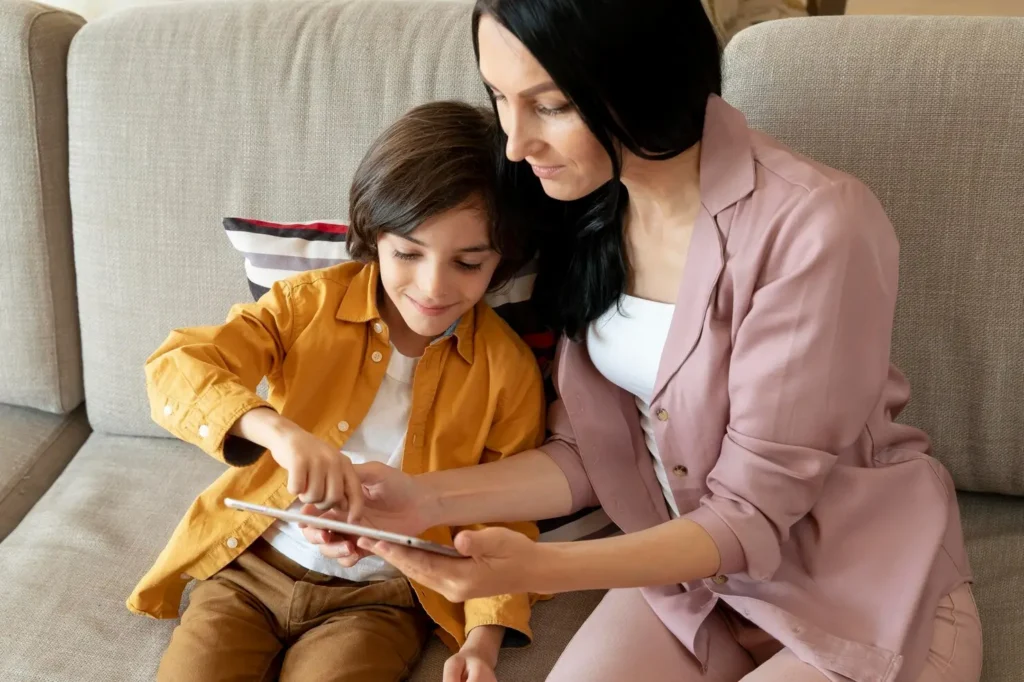 Parent and child sitting together on a couch looking at a tablet, reflecting guidance, shared learning, and attentive parenting.