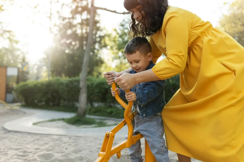 Mother helping her young son play on outdoor equipment at a park, illustrating hands-on parenting, stability, and the financial support that child support provides to help children thrive.