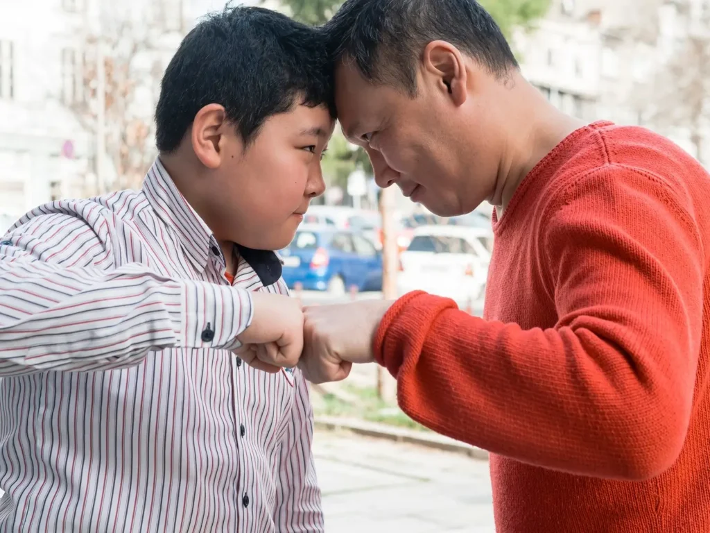 Father and son touching foreheads and bumping fists outdoors, symbolizing parental involvement, emotional connection, and the importance of consistent child support in a child’s life.