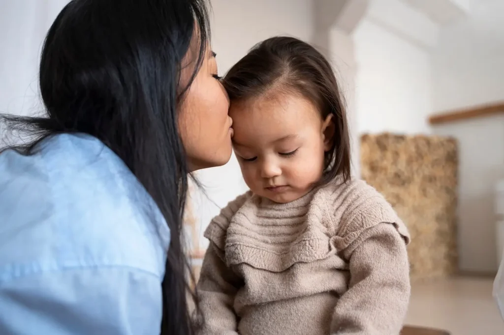 Mother gently kissing her young child on the forehead at home, symbolizing parental care, emotional security, and the financial stability that child support helps provide for a child’s well-being.