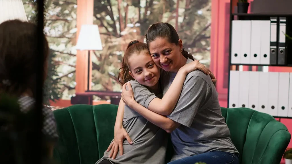 Mother and daughter hugging on a couch during a family meeting, representing emotional reassurance, stability, and the protective role child support plays in supporting a child’s well-being after separation.