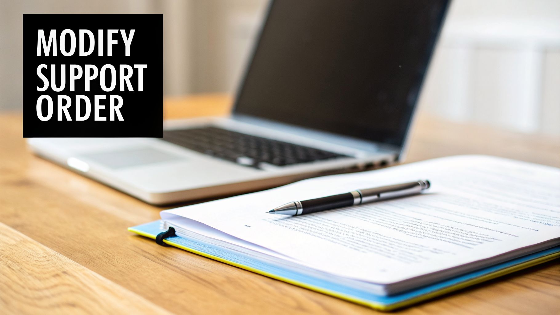 Desk with a laptop, paper, pen, and text overlay 'MODIFY SUPPORT ORDER' on a black background.