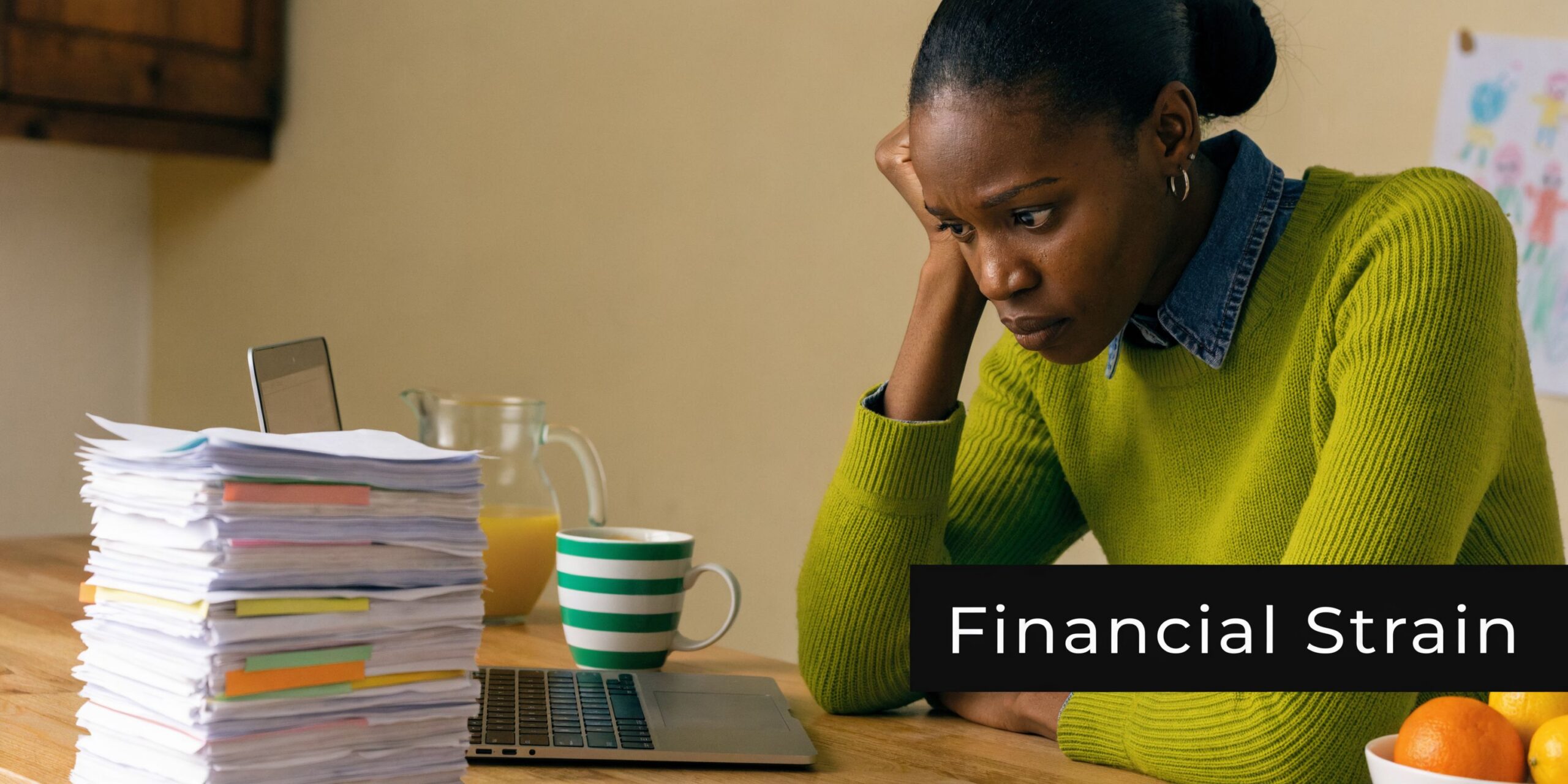 A stressed woman sitting at a desk with a large stack of paperwork and a laptop.