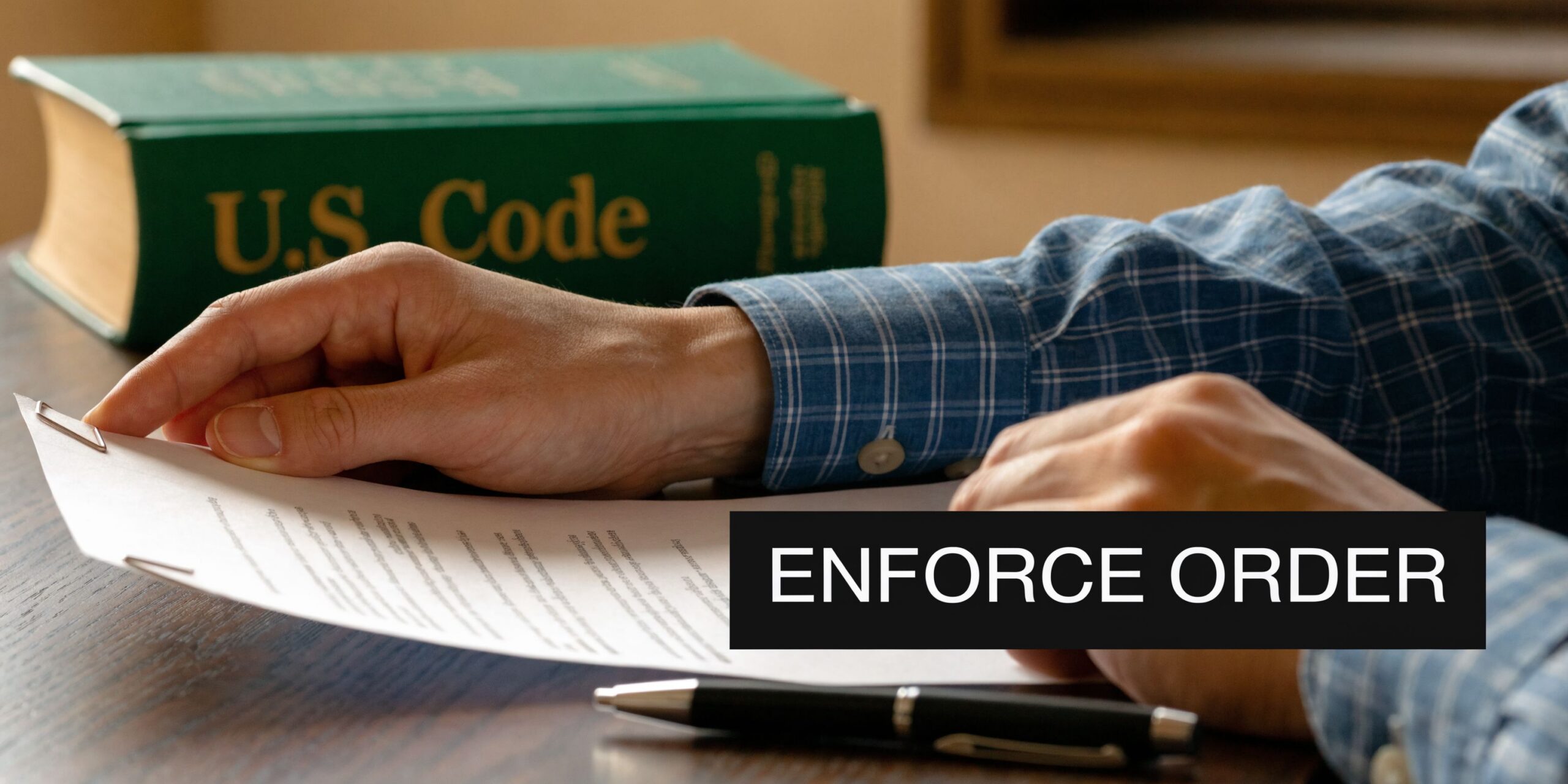 A person in a blue plaid shirt reading a legal document on a desk with a law book.