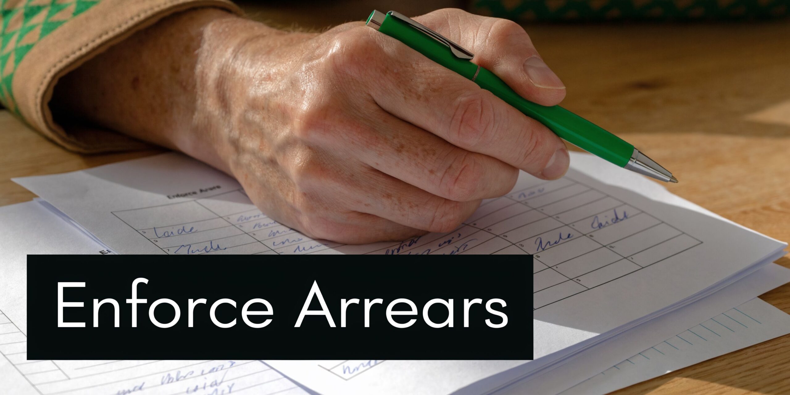 A close-up of a person's hand holding a green pen while filling out financial documentation paperwork.