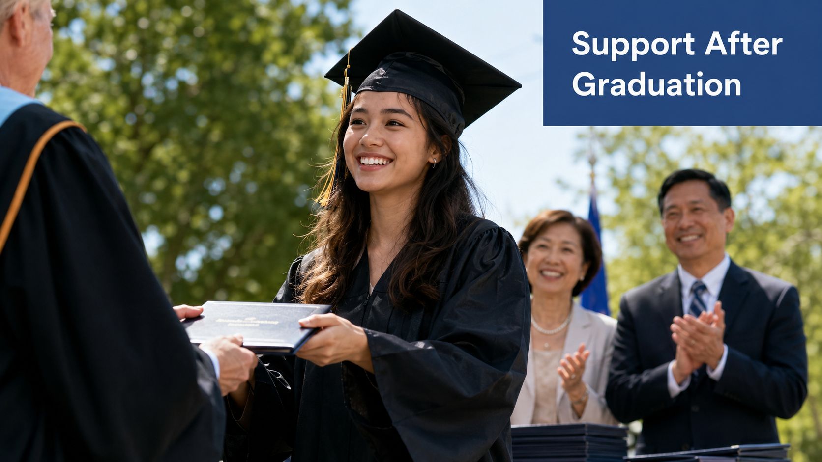 A smiling university graduate receiving her diploma during a commencement ceremony with parents watching in the background.